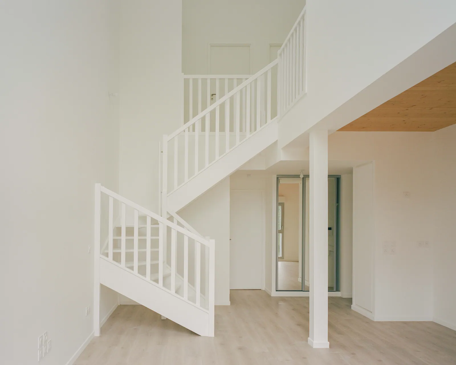 Escalier intérieur blanc dans un séjour en double hauteur, plafond bois apparent.