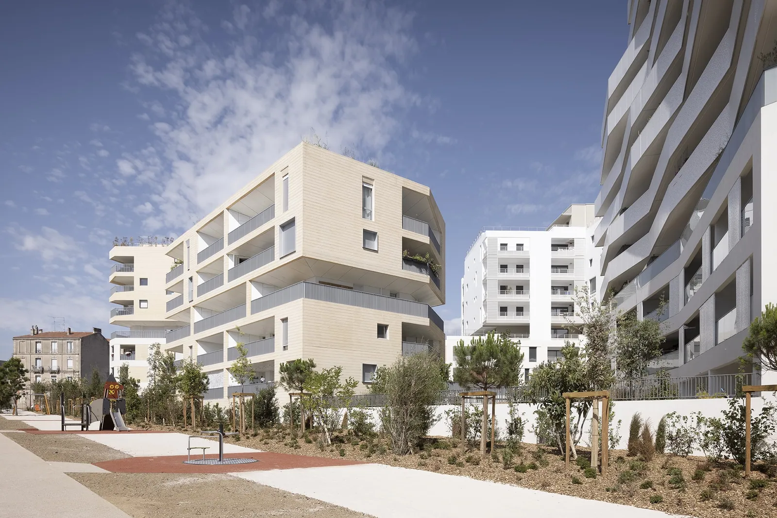 Carré Vendôme depuis le parc : volumes en béton matricé teinté et surfaces blanches lisses, terrasses en gradins, plantations méditerranéennes au premier plan.