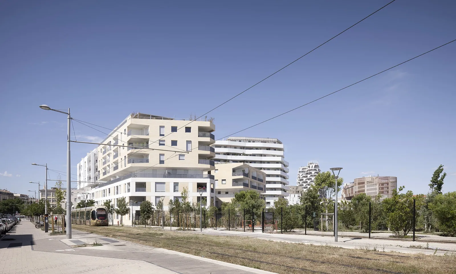 Le projet depuis la voie du tramway : volumes blancs et beiges en gradins dans le paysage urbain de la ZAC.