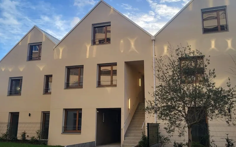 Les trois maisons à pignons en fin de journée : enduit clair, menuiseries bois, escalier extérieur et olivier planté au premier plan.