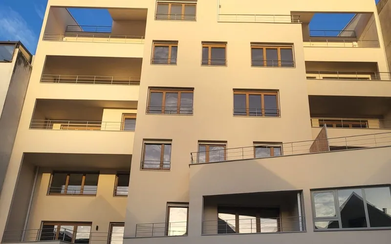 La façade sur cour en fin de journée : enduit clair, balcons filants et loggias profondes, grandes baies vitrées en rez-de-chaussée.